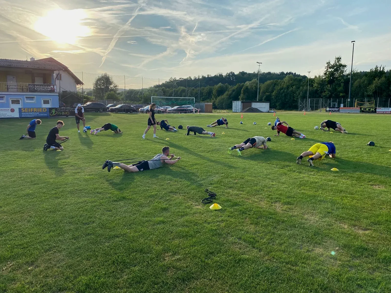 Gruppe beim Stabilisationstraining auf dem Fußballplatz bei Sonnenuntergang